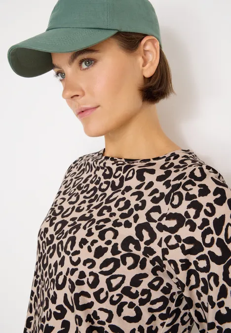 Frau mit grüner Kappe und Leopardenmuster-Shirt blickt zur Seite.